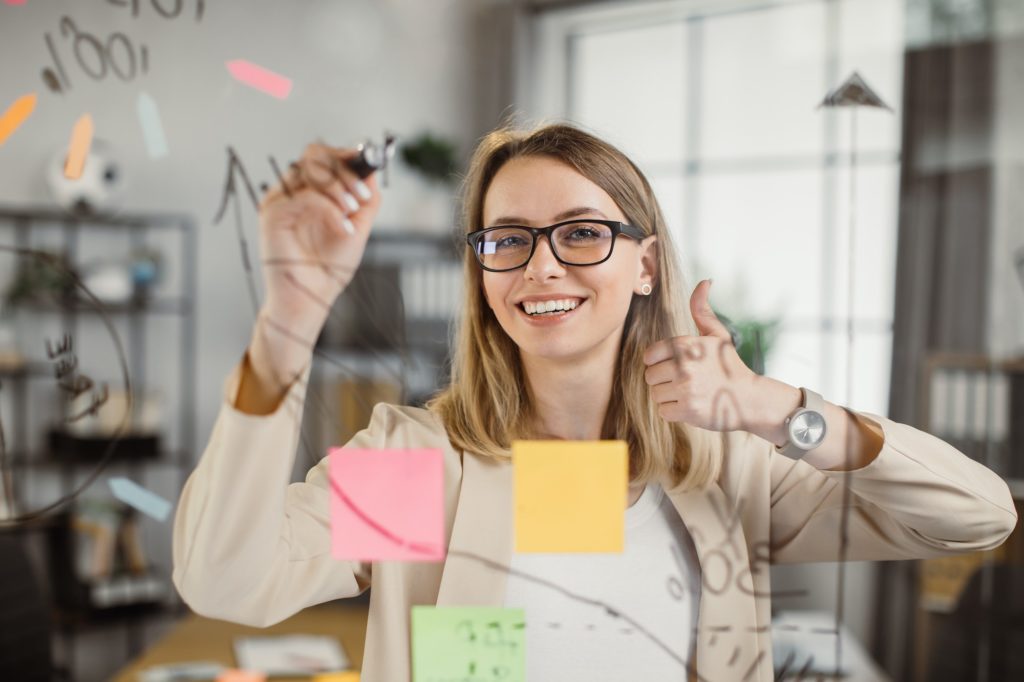 Female mentor showing thumb up while writing on board
